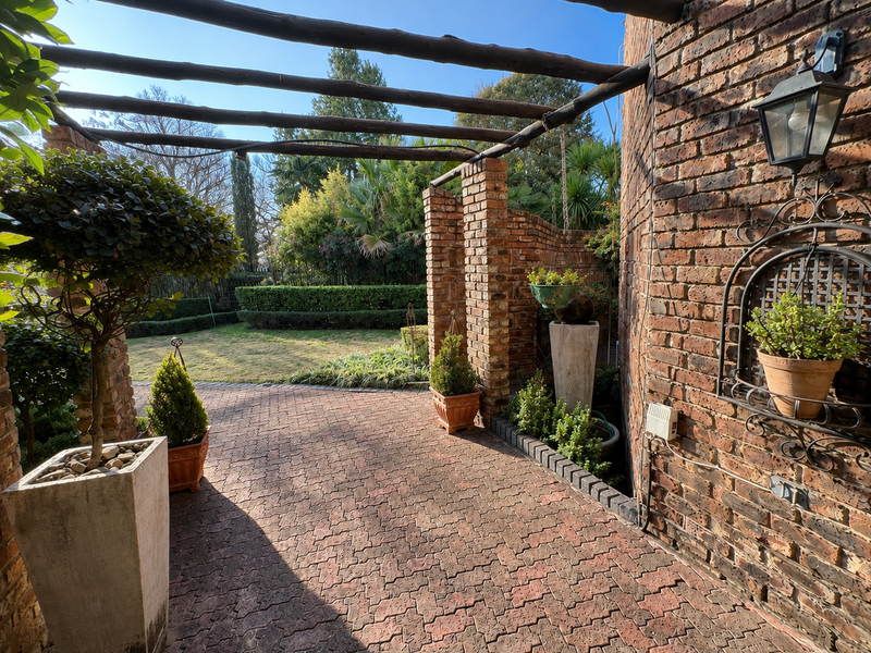 A charming covered patio area featuring rustic brick paving, exposed brick walls, and a timber pergola overlooking a well-maintained garden.