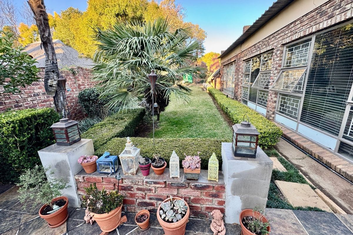 A well-maintained rear garden featuring a paved patio area, brick retaining wall, manicured hedging, and a lawn adjacent to the brick house exterior.