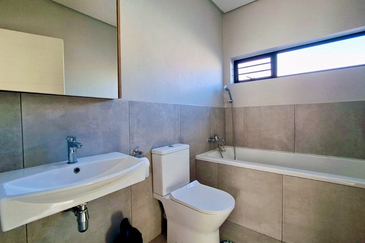 A modern, clean bathroom featuring large format wall tiles, a wall-mounted basin, a toilet, and a built-in bathtub with a handheld shower fixture.