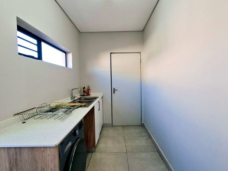 A clean and functional laundry room featuring built-in cabinetry, a stone countertop with a stainless steel sink, and modern tiled flooring.