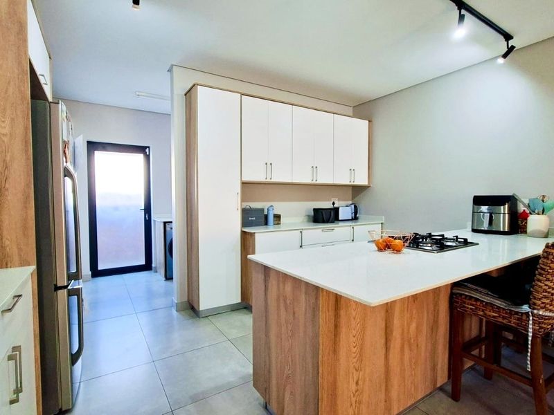 Modern kitchen featuring a central island with a gas hob, stone countertops, ample built-in cabinetry, and sleek track lighting.