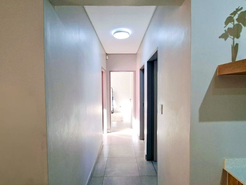 A clean, well-lit hallway featuring neutral wall tones and tiled flooring, providing access to multiple rooms within the home.