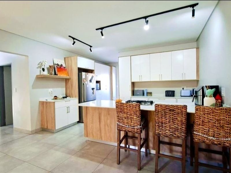 Modern kitchen featuring light wood and white cabinetry, a central island with a gas hob, stone countertops, and contemporary track lighting.