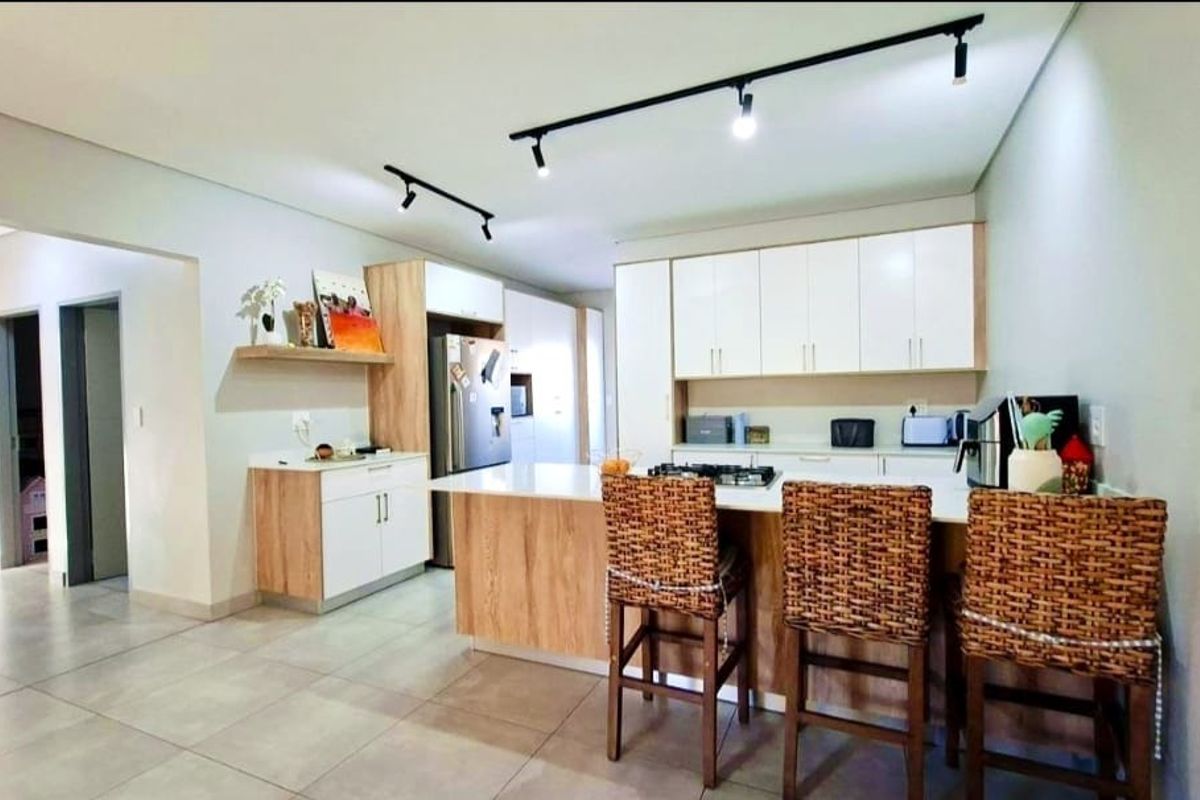 Modern kitchen featuring light wood and white cabinetry, a central island with a gas hob, stone countertops, and contemporary track lighting.