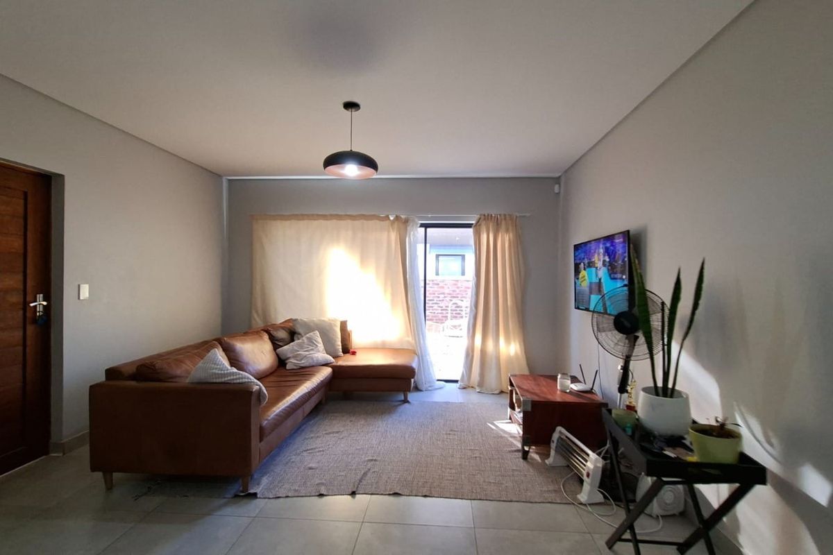 A well-lit living room featuring neutral tiled flooring and a sliding glass door providing access to the outdoor area.