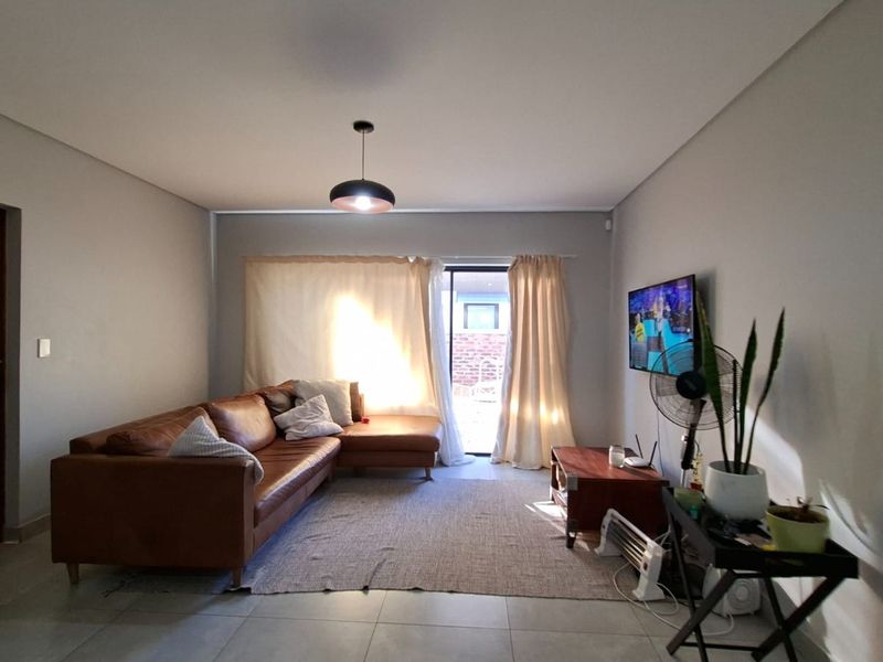 A well-lit living room featuring neutral tiled flooring and a sliding glass door providing access to the outdoor area.