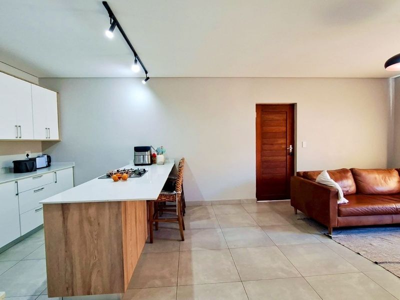 Modern open-plan living area featuring a sleek kitchen with stone countertops, gas hob, island seating, and neutral tiled flooring throughout.