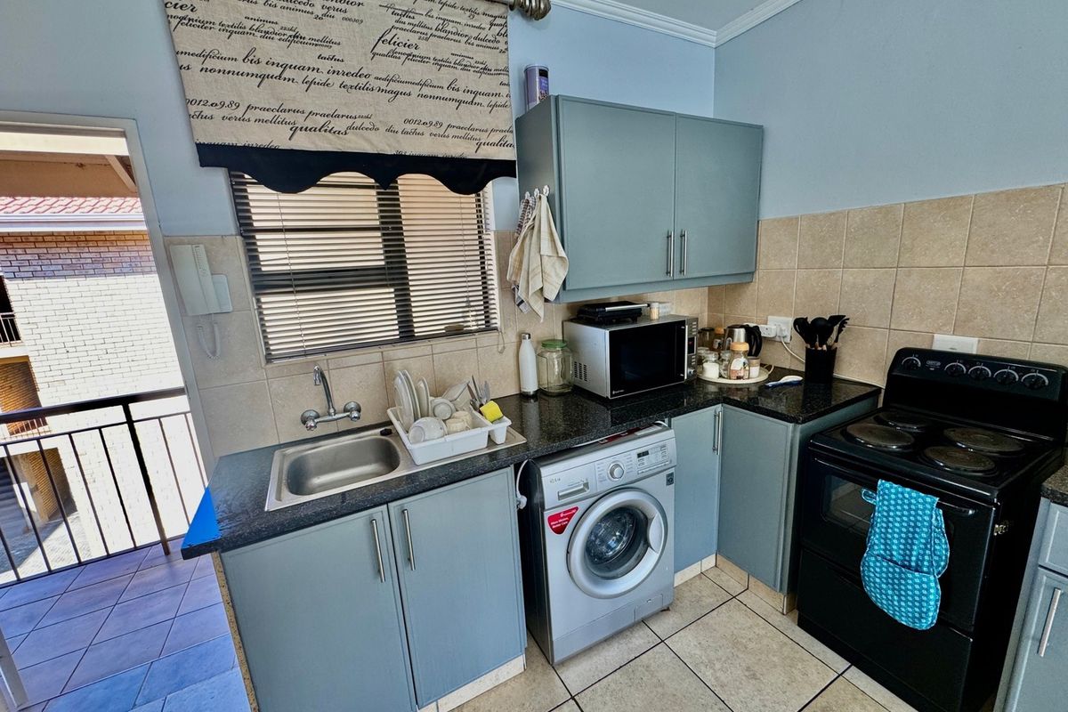 Compact kitchen featuring built-in cabinetry, granite countertops, tiled backsplash, and space for a washing machine, with direct access to an outdoor balcony area.