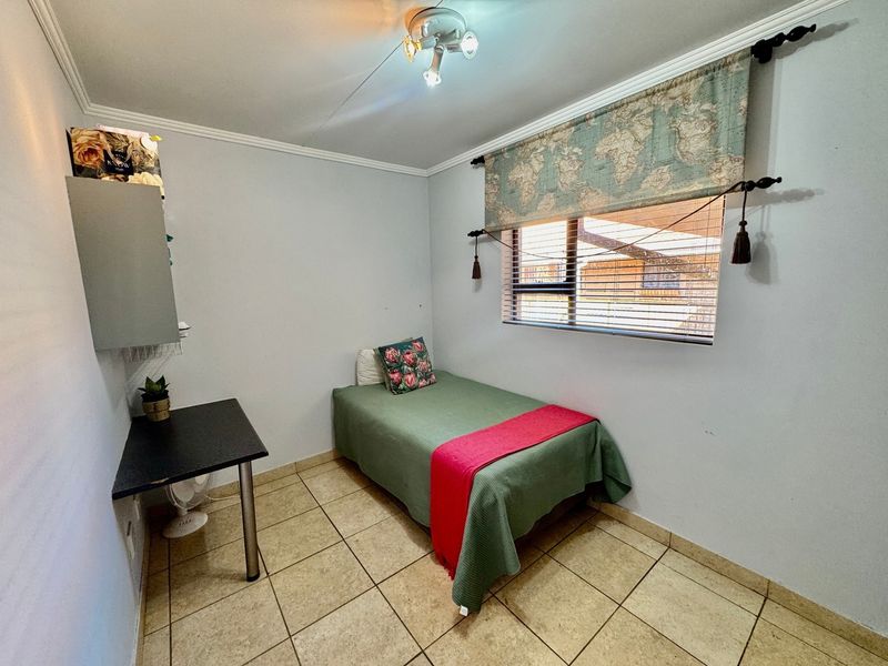 A compact bedroom featuring tiled flooring, a window with fitted blinds, and wall-mounted storage shelving.