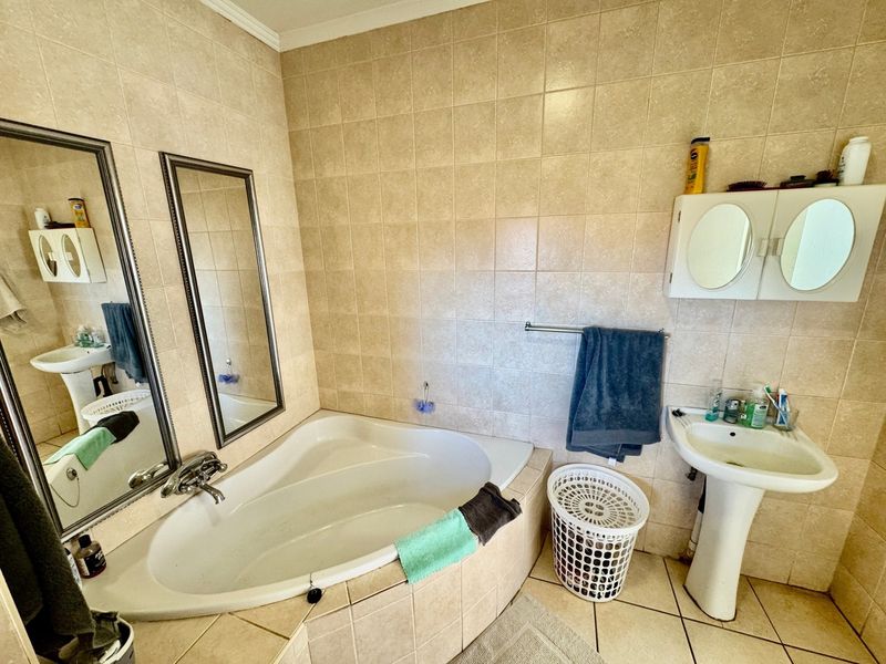 A functional bathroom featuring a corner bathtub, pedestal basin, and wall-mounted medicine cabinet with neutral tiled finishes throughout.