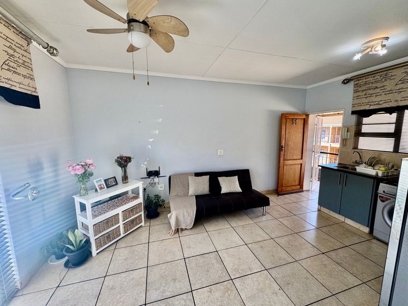 Open-plan living area featuring tiled flooring, a ceiling fan, and a compact kitchen corner with built-in cabinetry and sink.