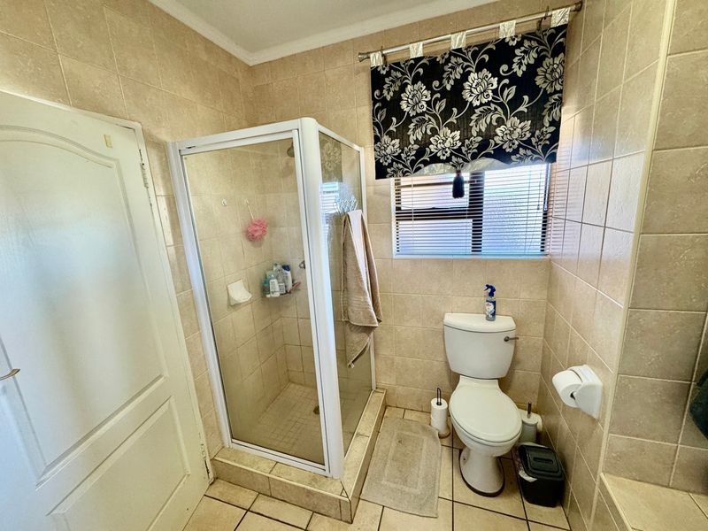 A functional bathroom featuring a corner shower enclosure, a standard toilet, and neutral wall and floor tiling.