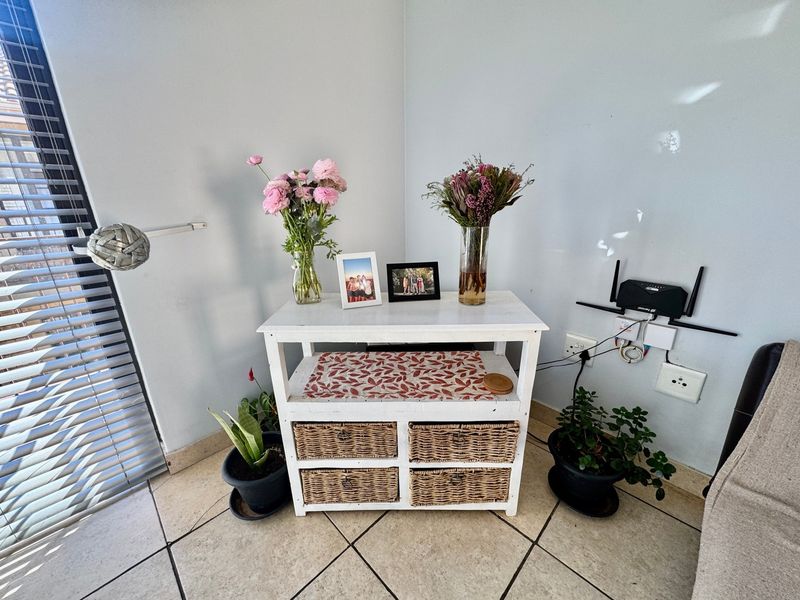 A corner view of a living area featuring tiled flooring and venetian blinds, providing a neutral space for potential interior design updates.