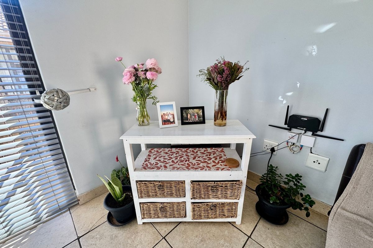 A corner view of a living area featuring tiled flooring and venetian blinds, providing a neutral space for potential interior design updates.