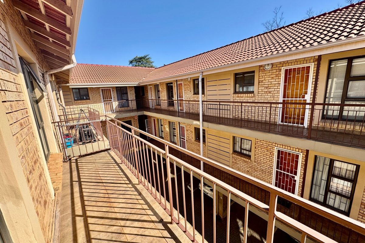 An exterior view of an apartment complex featuring brick facades, tiled roofing, and metal balcony railings overlooking a central courtyard area.