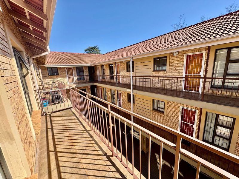 An exterior view of an apartment complex featuring brick facades, tiled roofing, and metal balcony railings overlooking a central courtyard area.