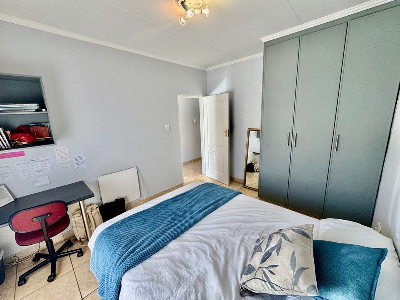 A well-maintained bedroom featuring built-in cupboards, tiled flooring, and a functional layout with integrated shelving.