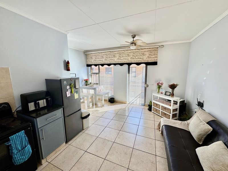 Open-plan living and kitchen area featuring tiled flooring, a ceiling fan, and functional kitchen cabinetry with granite countertops.