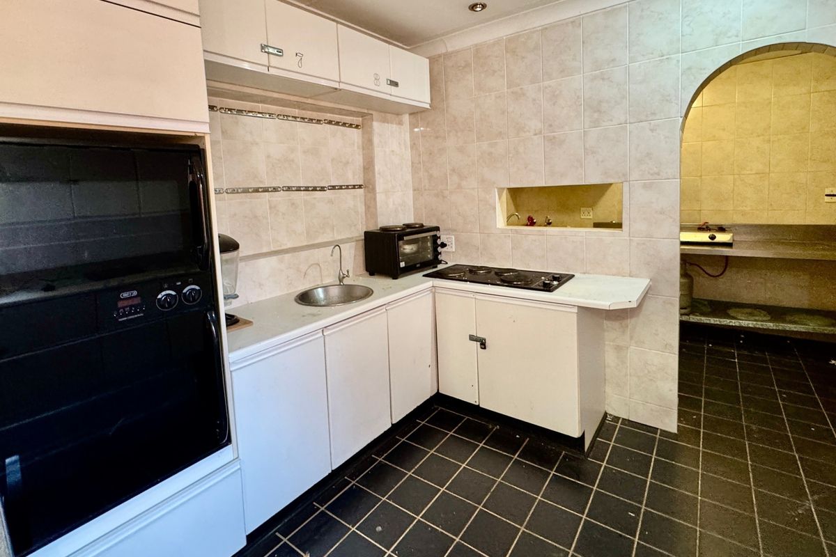 A functional kitchen featuring built-in cabinetry, an oven, a hob, and a tiled splashback, with an arched opening leading to an adjacent utility area.