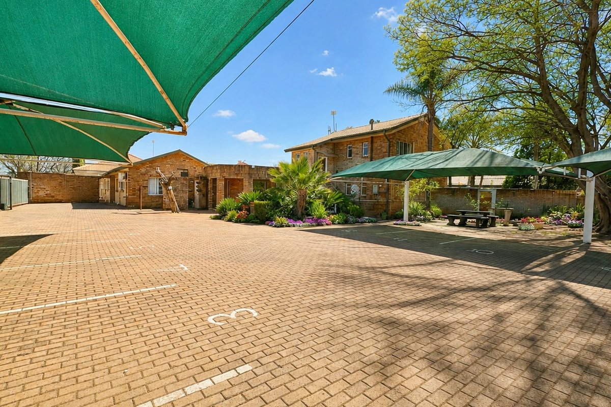 Spacious paved parking area featuring multiple shade sails, established garden beds, and brick boundary walls, providing ample outdoor space for vehicles.