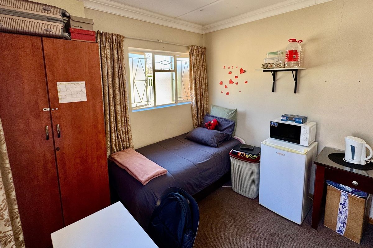 A compact bedroom featuring carpet flooring, a built-in wardrobe, and a window fitted with security bars.