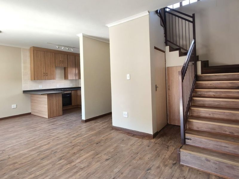 Open-plan living area featuring laminate flooring, a functional kitchen with built-in cabinetry, and a staircase leading to the upper level.