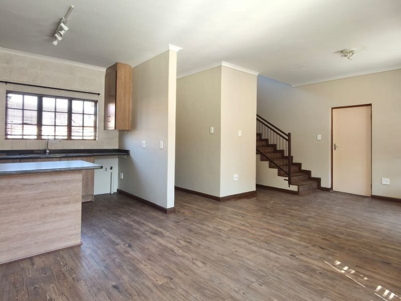 Spacious open-plan living area featuring laminate flooring, a functional kitchen with peninsula, and a staircase leading to the upper level.