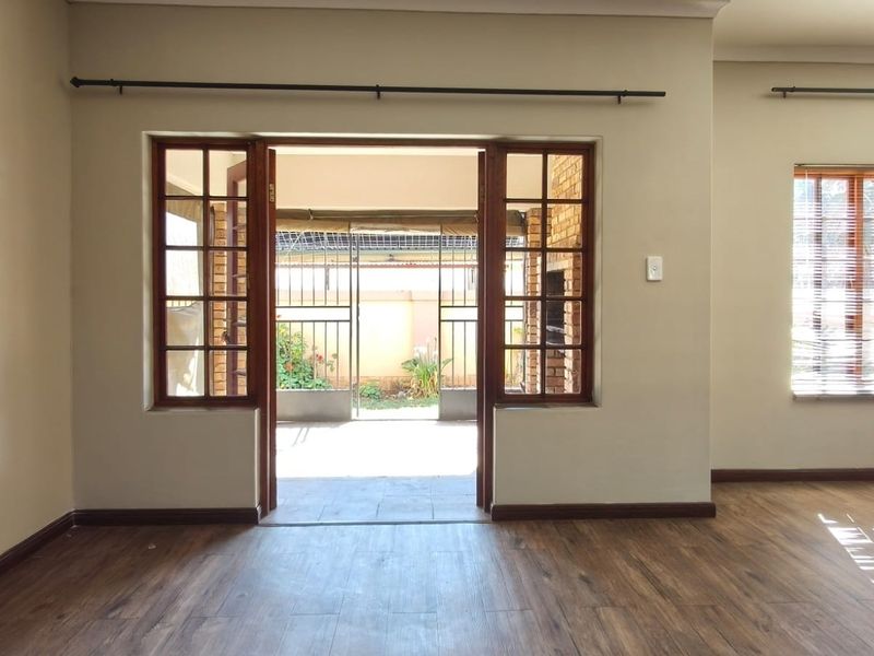Spacious living area featuring timber-framed glass doors opening to an outdoor patio, complemented by warm-toned laminate flooring and neutral wall finishes.