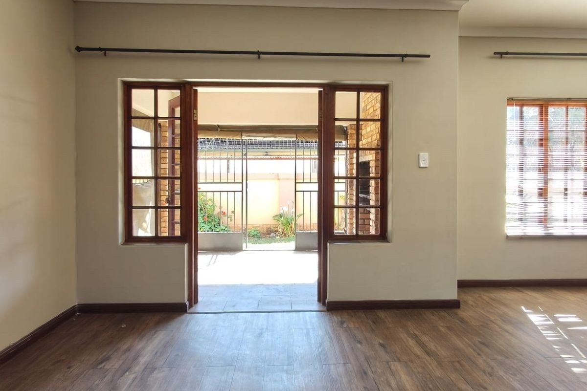 Spacious living area featuring timber-framed glass doors opening to an outdoor patio, complemented by warm-toned laminate flooring and neutral wall finishes.