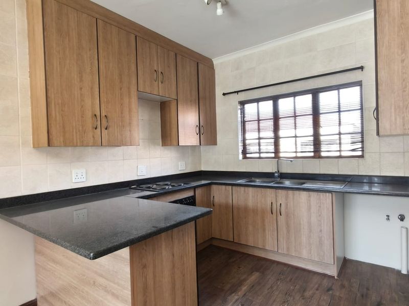 A clean, functional kitchen featuring wood-look laminate cabinetry, dark granite countertops, a built-in hob, and a double sink with a tiled backsplash.