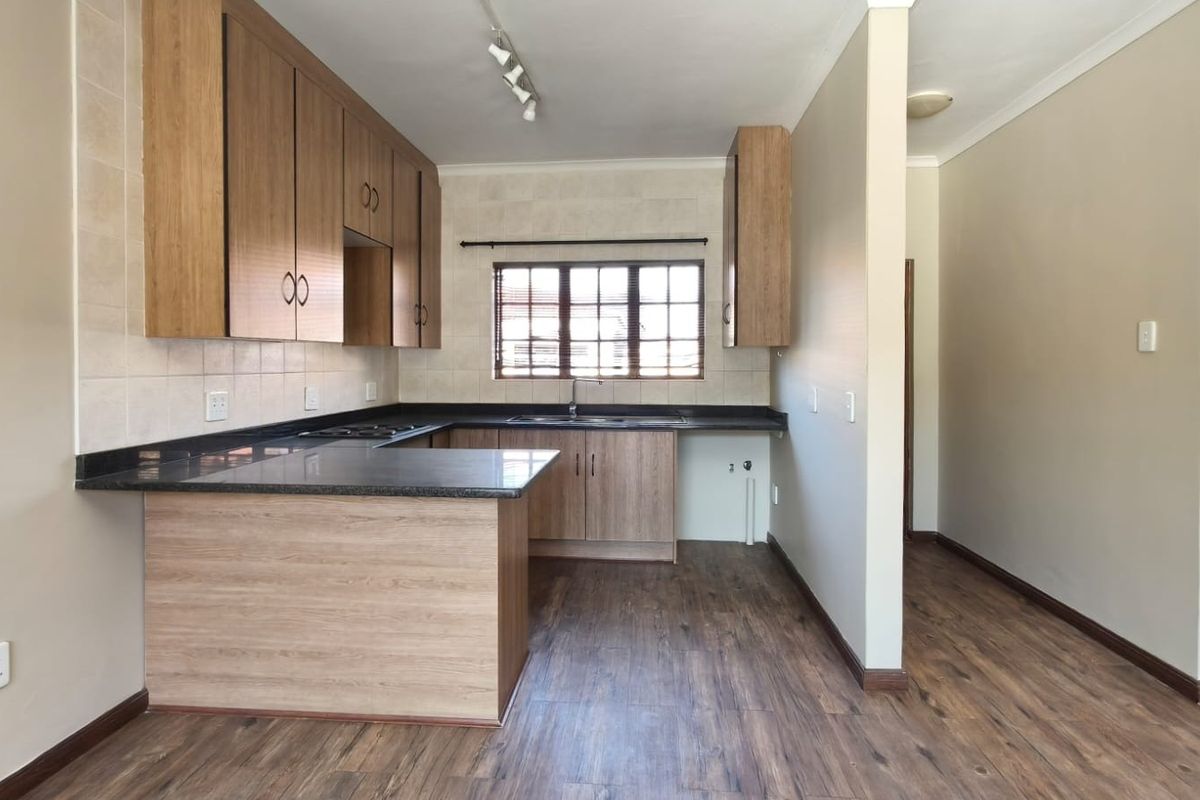 A clean, functional kitchen featuring wood-look laminate cabinetry, dark granite countertops, a double sink, and integrated hob with tiled backsplash.