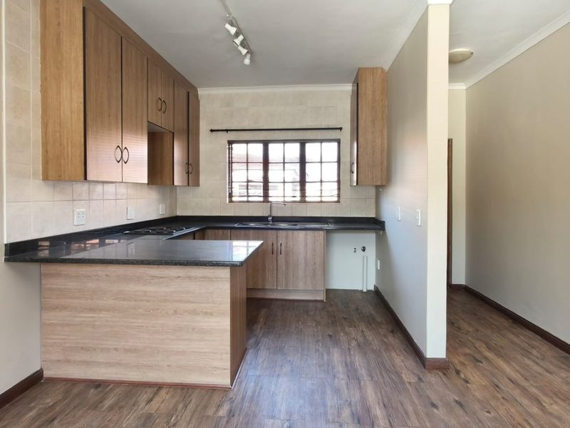 A clean, functional kitchen featuring wood-look laminate cabinetry, dark granite countertops, a double sink, and integrated hob with tiled backsplash.