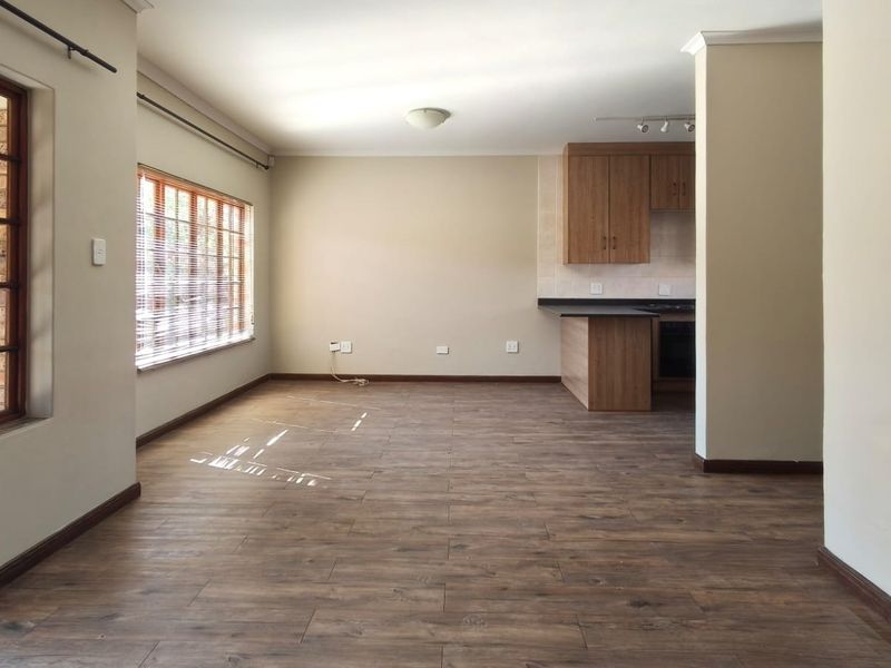 An open-plan living and kitchen area featuring laminate flooring, timber-framed windows, and functional built-in cabinetry with integrated cooking appliances.