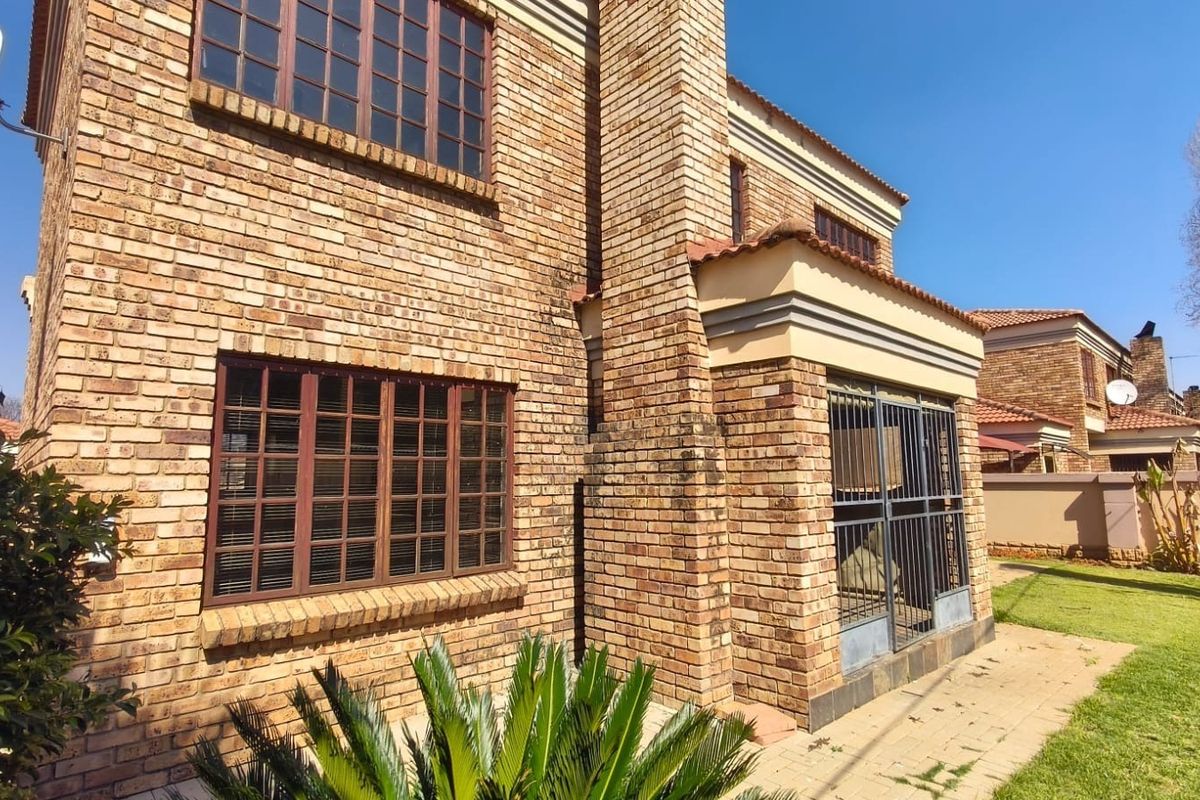 Rear view of a face brick townhouse featuring a paved patio area, security gate, and established lawn.