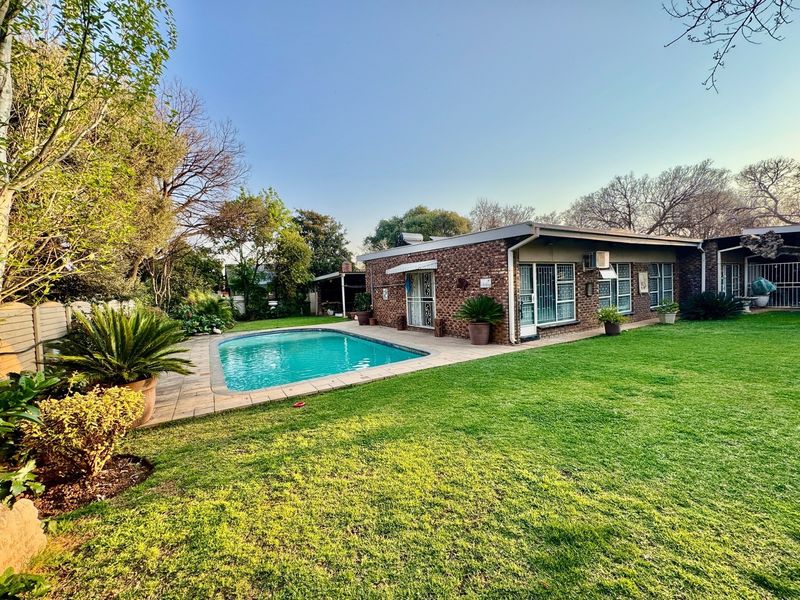 A well-maintained rear garden featuring a swimming pool, paved surround, and a brick-clad house exterior with security features.