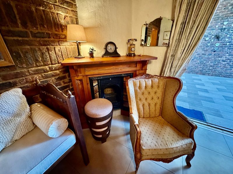 A cozy living area featuring an exposed brick wall, a traditional wooden fireplace mantel with a cast iron insert, and access to an outdoor patio.