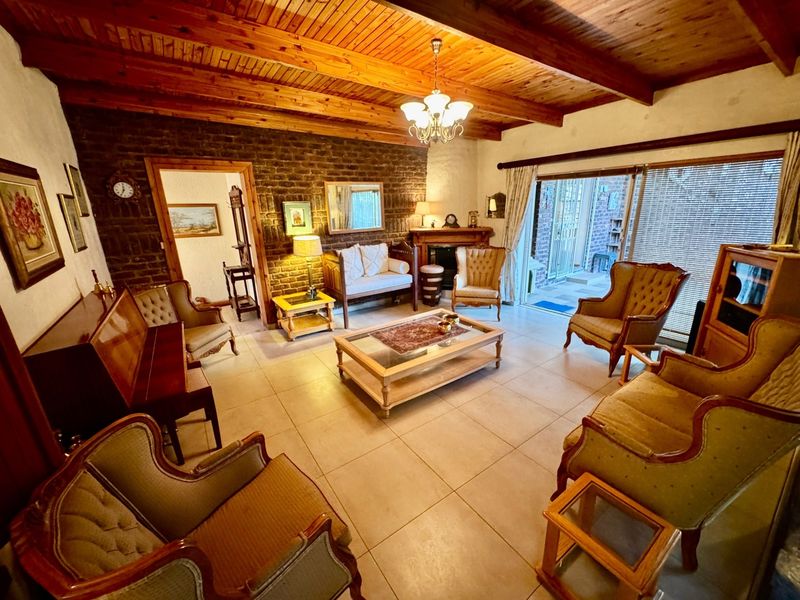 Spacious living room featuring an exposed timber beam ceiling, a rustic brick feature wall, a fireplace, and large sliding doors leading to the patio.