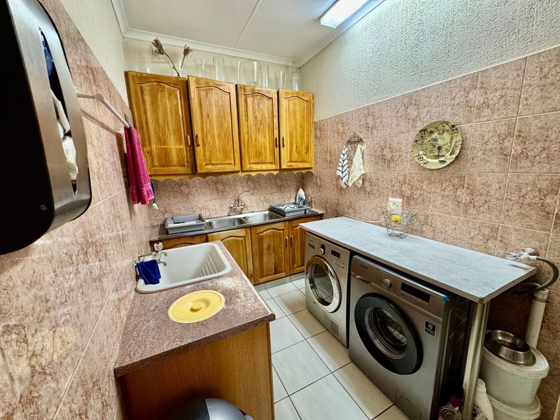 A functional laundry room featuring built-in wooden cabinetry, a double stainless steel sink, a separate utility sink, and tiled finishes throughout.