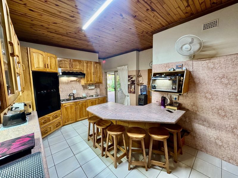 A functional kitchen featuring wooden cabinetry, tiled countertops, a built-in oven, gas hob, and a timber ceiling with direct access to the outdoor area.
