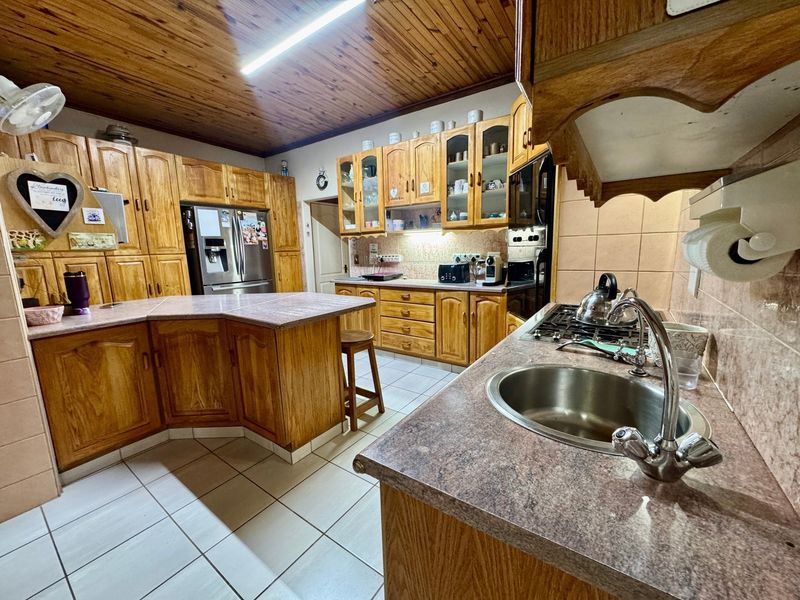 A spacious kitchen featuring extensive wooden cabinetry, laminate countertops, a gas hob, and a distinctive timber-paneled ceiling with tiled flooring.