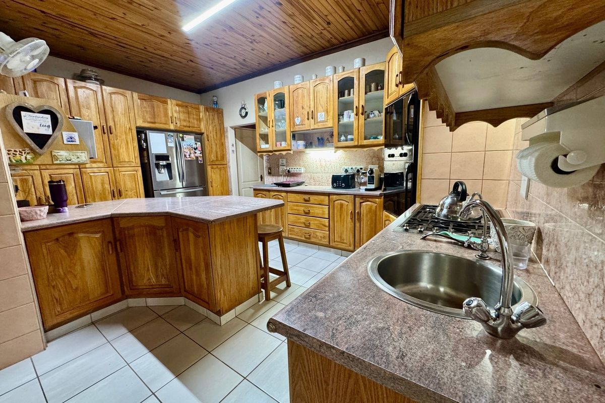 A spacious kitchen featuring extensive wooden cabinetry, laminate countertops, a gas hob, and a distinctive timber-paneled ceiling with tiled flooring.
