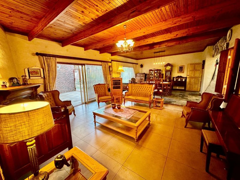 Spacious open-plan living and dining area featuring exposed timber beam ceilings, tiled flooring, and direct access to an outdoor patio through sliding glass doors.