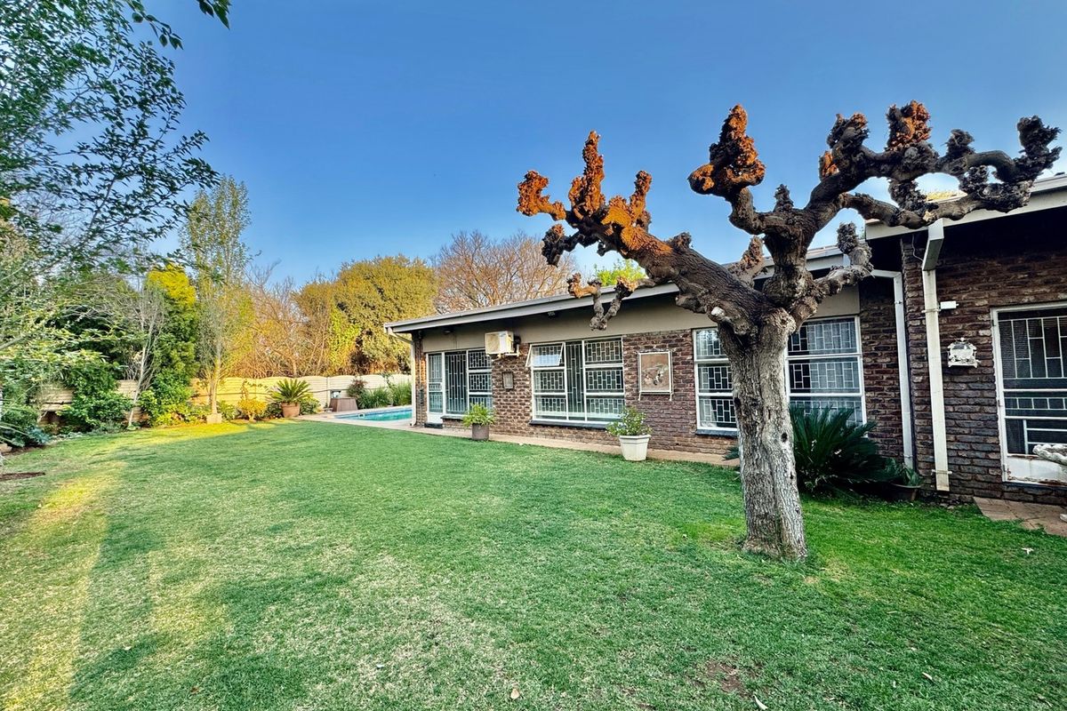 Rear view of the property featuring a brick facade, security-barred windows, a well-maintained lawn, and a swimming pool in the background.