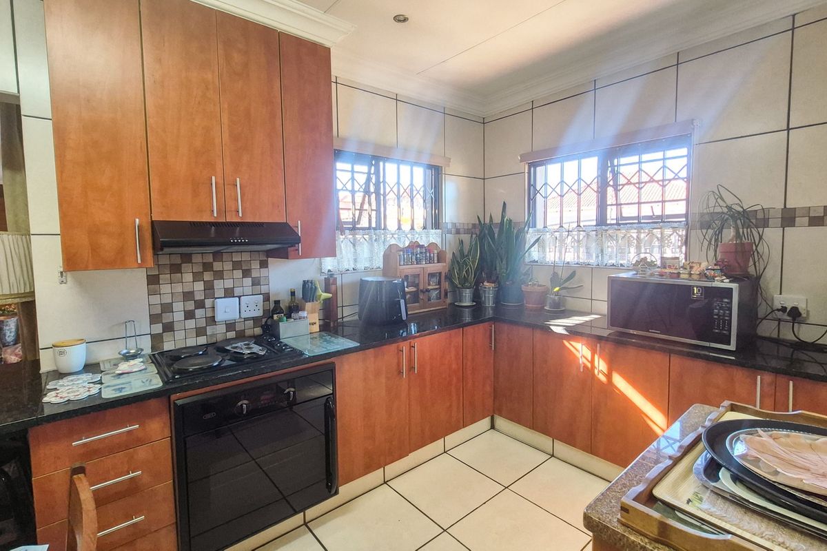 Functional kitchen featuring wood-finish cabinetry, granite countertops, built-in oven, gas hob, and tiled splashbacks with ample natural light.
