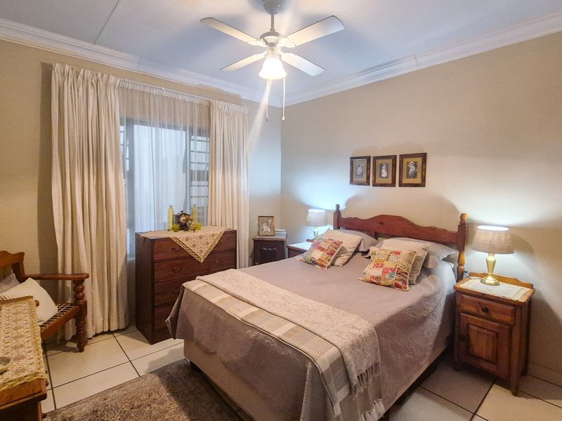 A well-lit bedroom featuring tiled flooring, a ceiling fan, and built-in storage, offering a comfortable and functional living space.