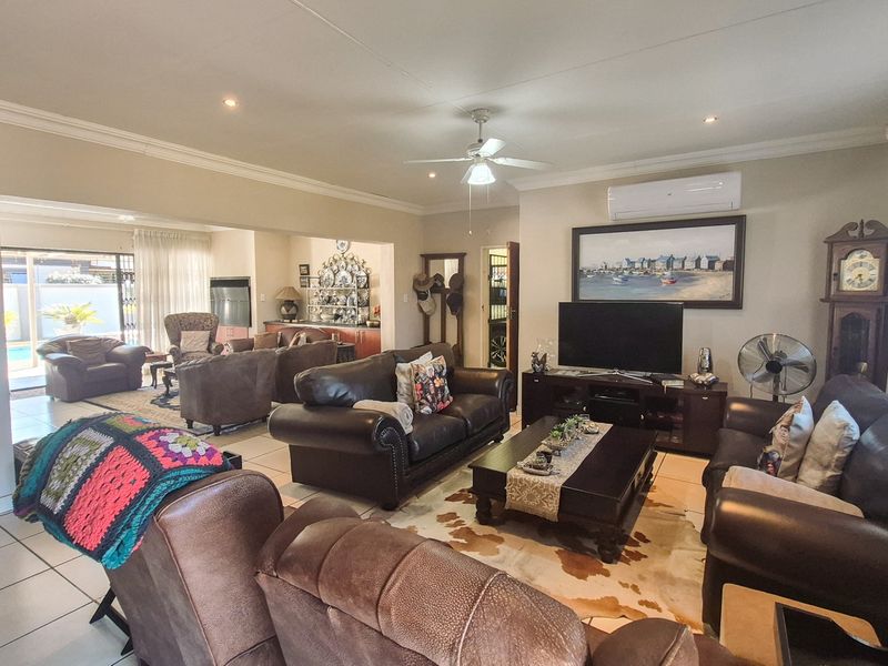 Spacious open-plan living area featuring tiled flooring, crown molding, a ceiling fan, and a wall-mounted split-system air conditioner.