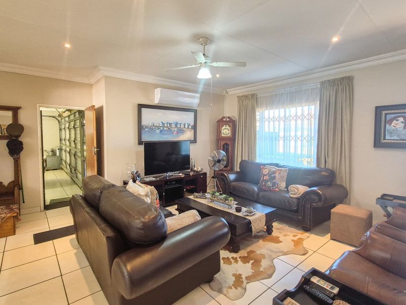 Spacious living room featuring tiled flooring, a ceiling fan, and a wall-mounted air conditioning unit, providing a comfortable and functional family space.