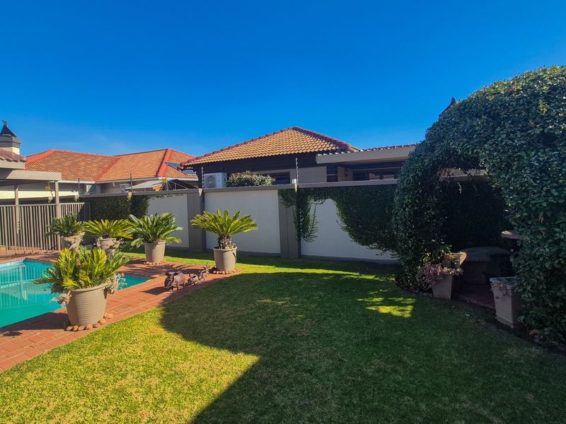 A well-maintained outdoor pool area featuring a swimming pool, brick paved surround, and established garden landscaping within a secure perimeter wall.