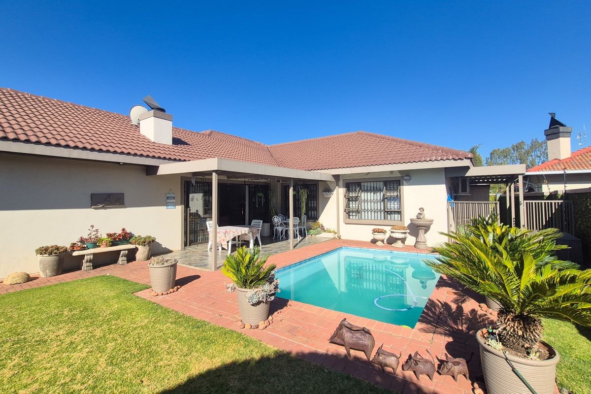 Rear exterior view of the townhouse featuring a swimming pool, covered patio area, brick paving, and well-maintained garden surroundings.