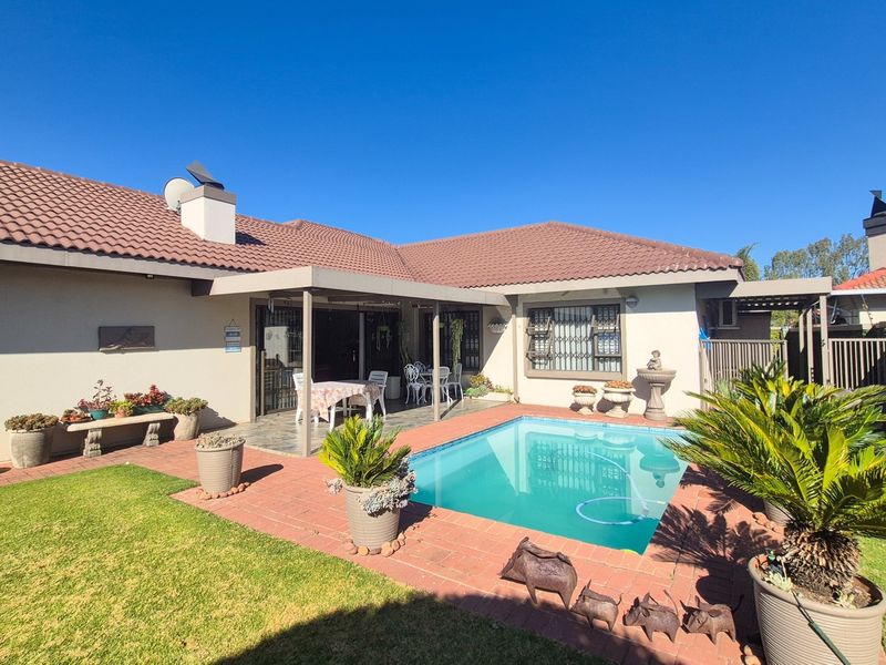 Rear exterior view of the townhouse featuring a swimming pool, covered patio area, brick paving, and well-maintained garden surroundings.